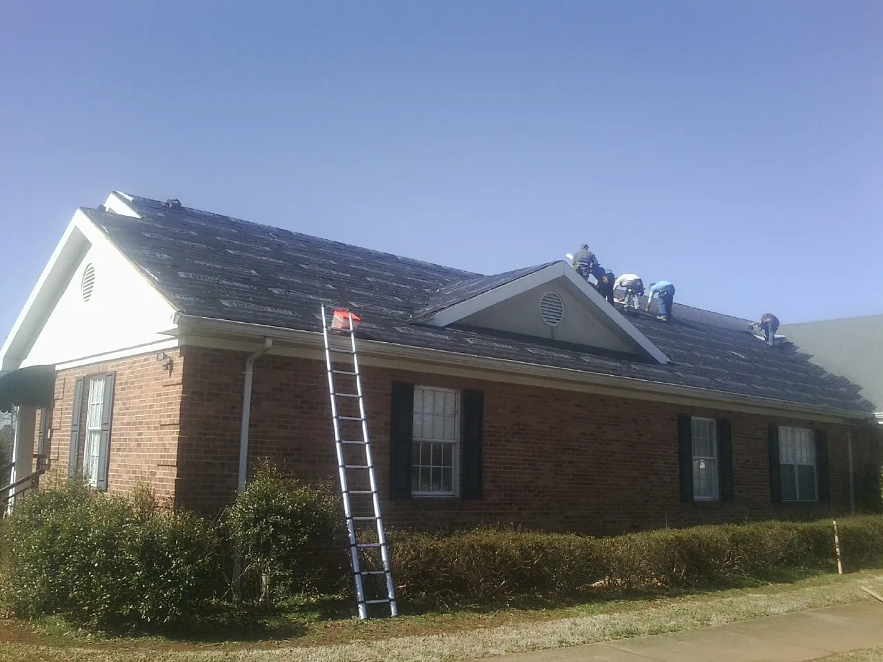 Crew tearing shingles off a brick ranch roof with a ladder set — Emergency Roof Repair work by our crew in Agency