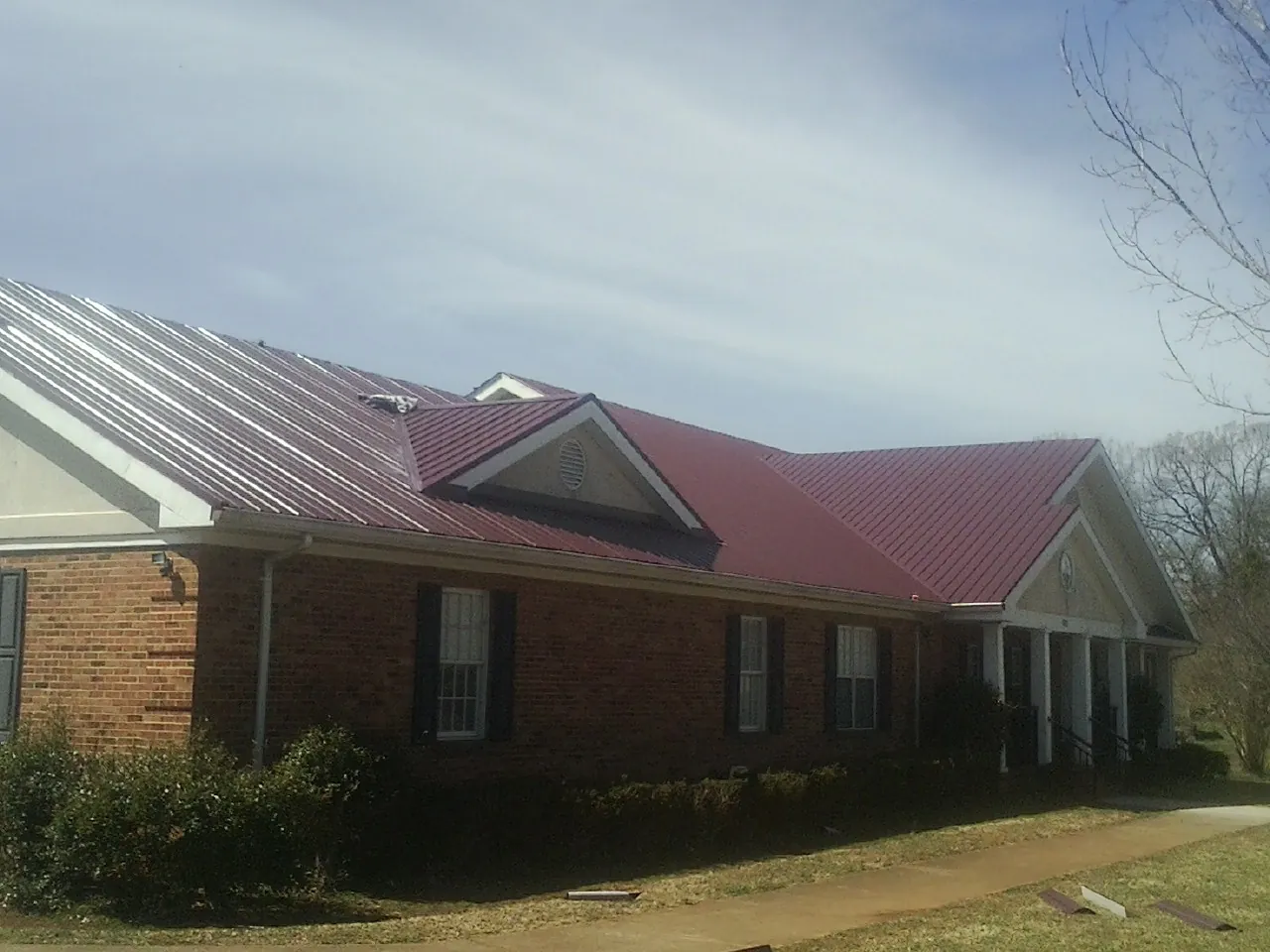 Red metal roof with gabled entries on a long brick building, from a Hail Damage Roof Repair job in Agency