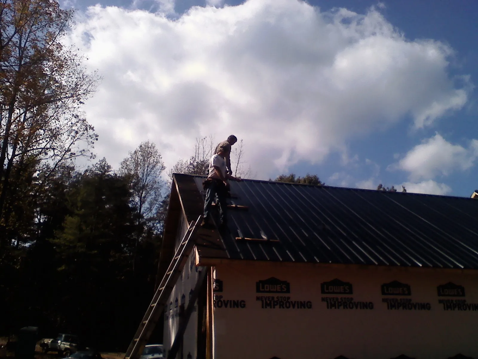 Roofer fastening dark metal panels high against a cloudy sky, from a Roof Inspection job in Agency