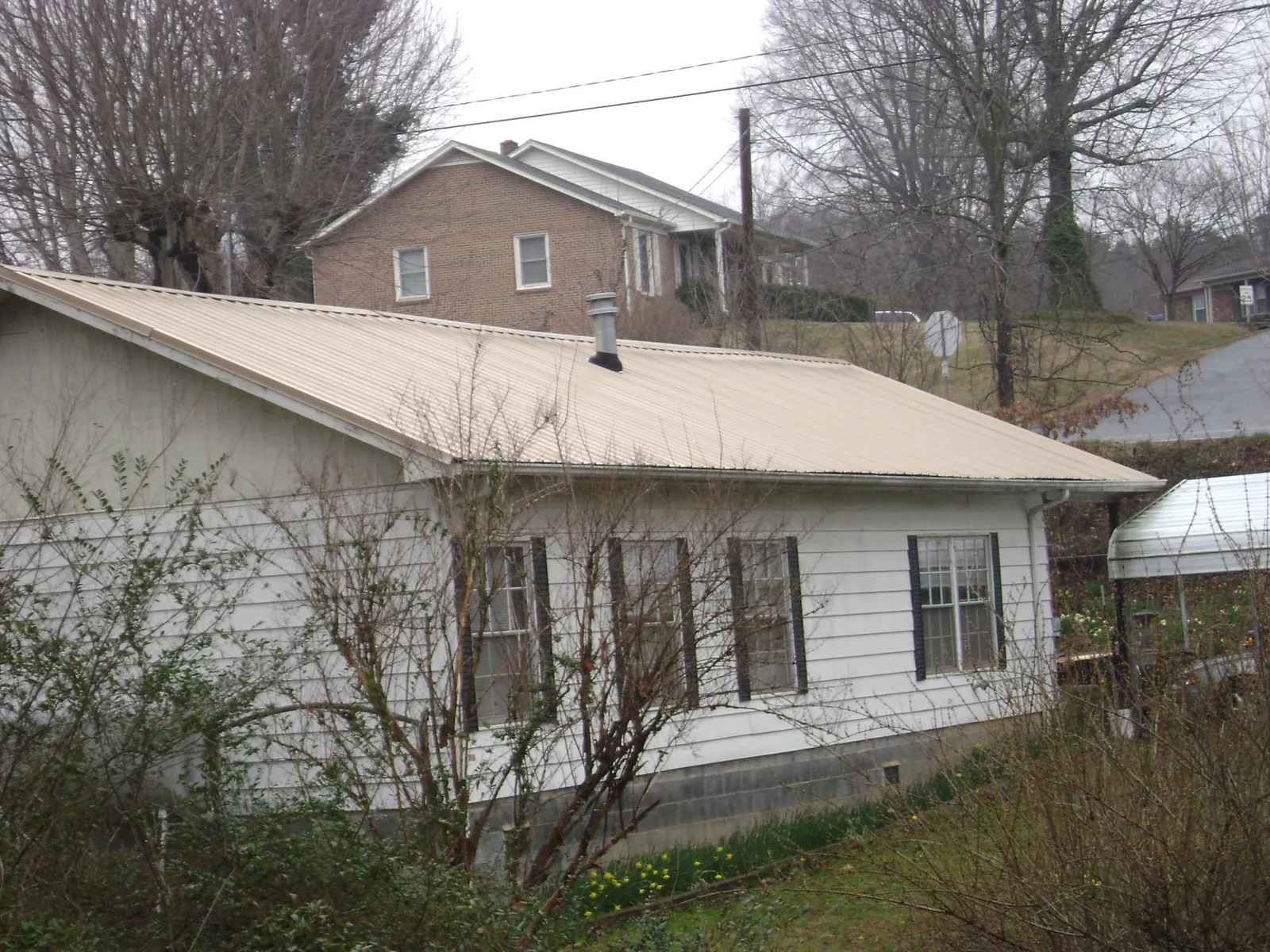 Tan metal roof on a white sided house set into a hillside in Agency